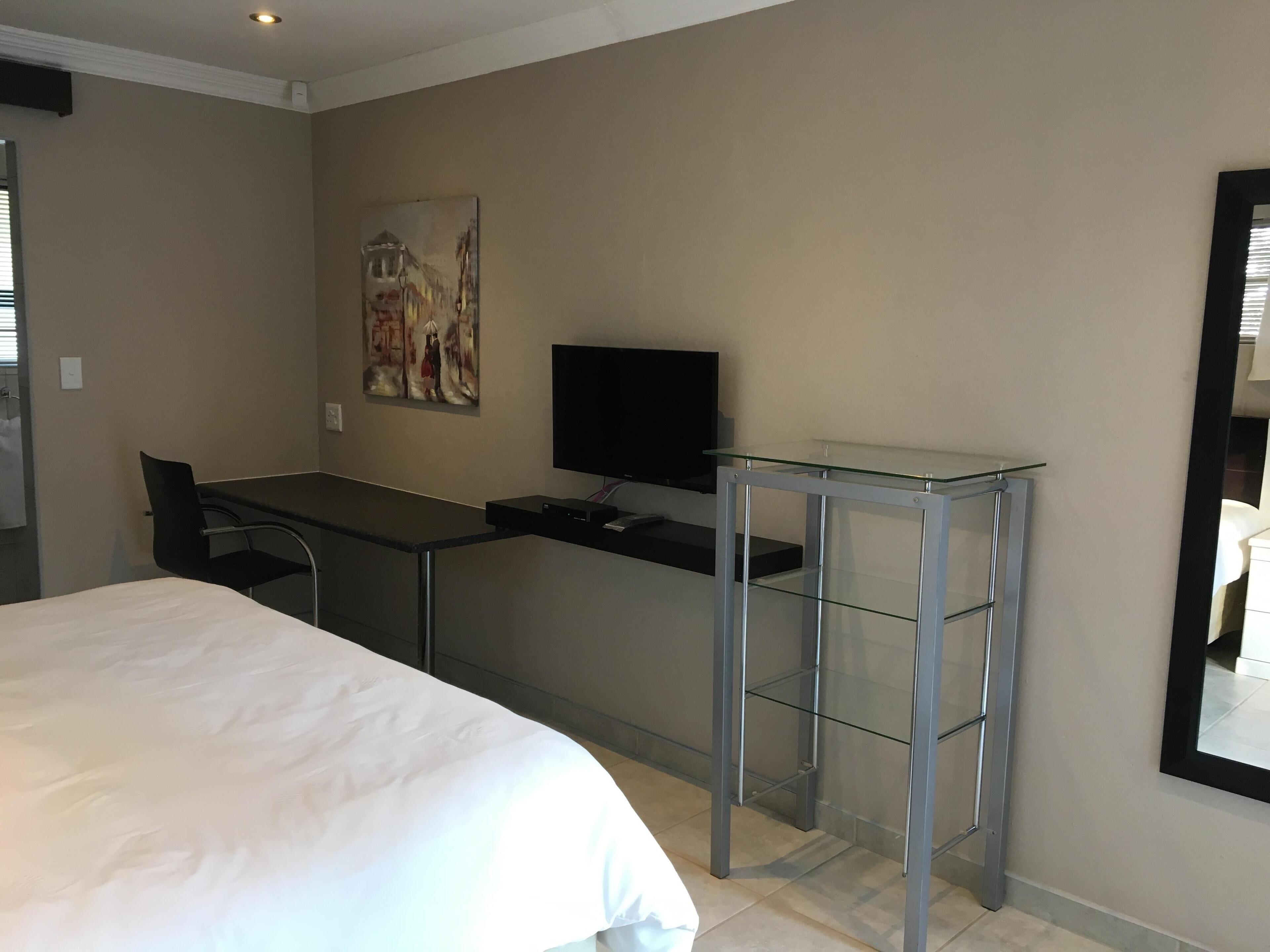 Une chambre d’hôtel comprenant un lit, un bureau, une chaise, un téléviseur et une table en verre.