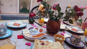 A dining table set with traditional Moroccan dishes, a vase of flowers, and a candle. - Dar Halima (Marrakech)