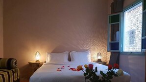 A hotel room with a bed, bedside tables, a small table with drinks, and a window with decorative bars. - Dar Halima (Marrakech)