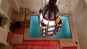 A room with a colorful mosaic lantern hanging above a blue pool, a red patterned rug, and a beige sofa with striped cushions. - Dar Halima (Marrakech)