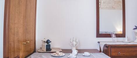 A wooden table with a placemat, a plate of cookies, a white pitcher, and two cups. A mirror and a television are mounted on the wall above the table.