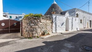 A stone wall with a cactus, a white building with a conical roof, and a gated entrance. - Trullieu Guesthouse (Alberobello)