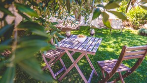 A wooden table with two chairs, a bowl of bread, and two wine glasses in a garden setting. - Trullieu Guesthouse (Alberobello)