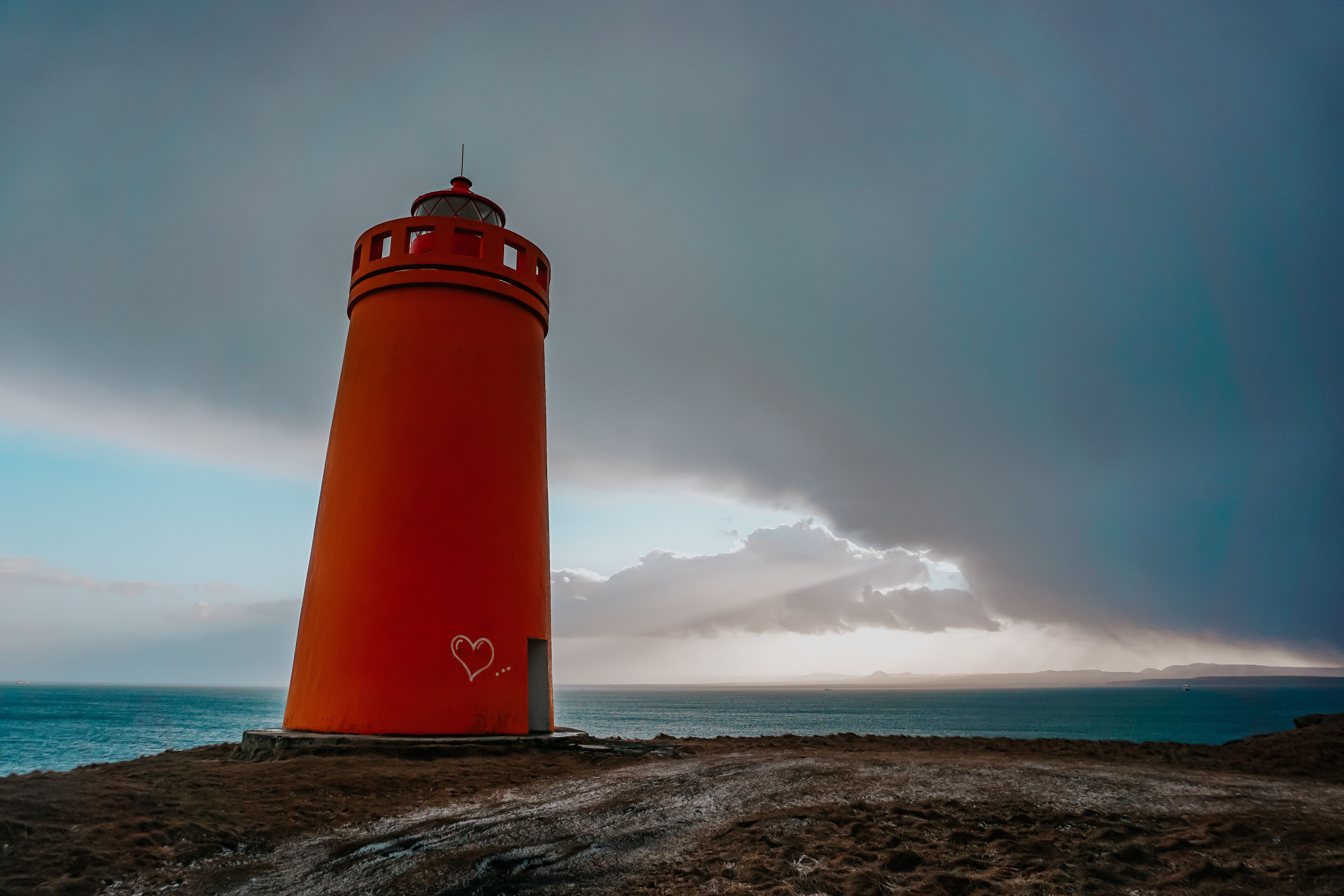 Um farol vermelho numa praia arenosa, com vista para o oceano e um céu nublado.
