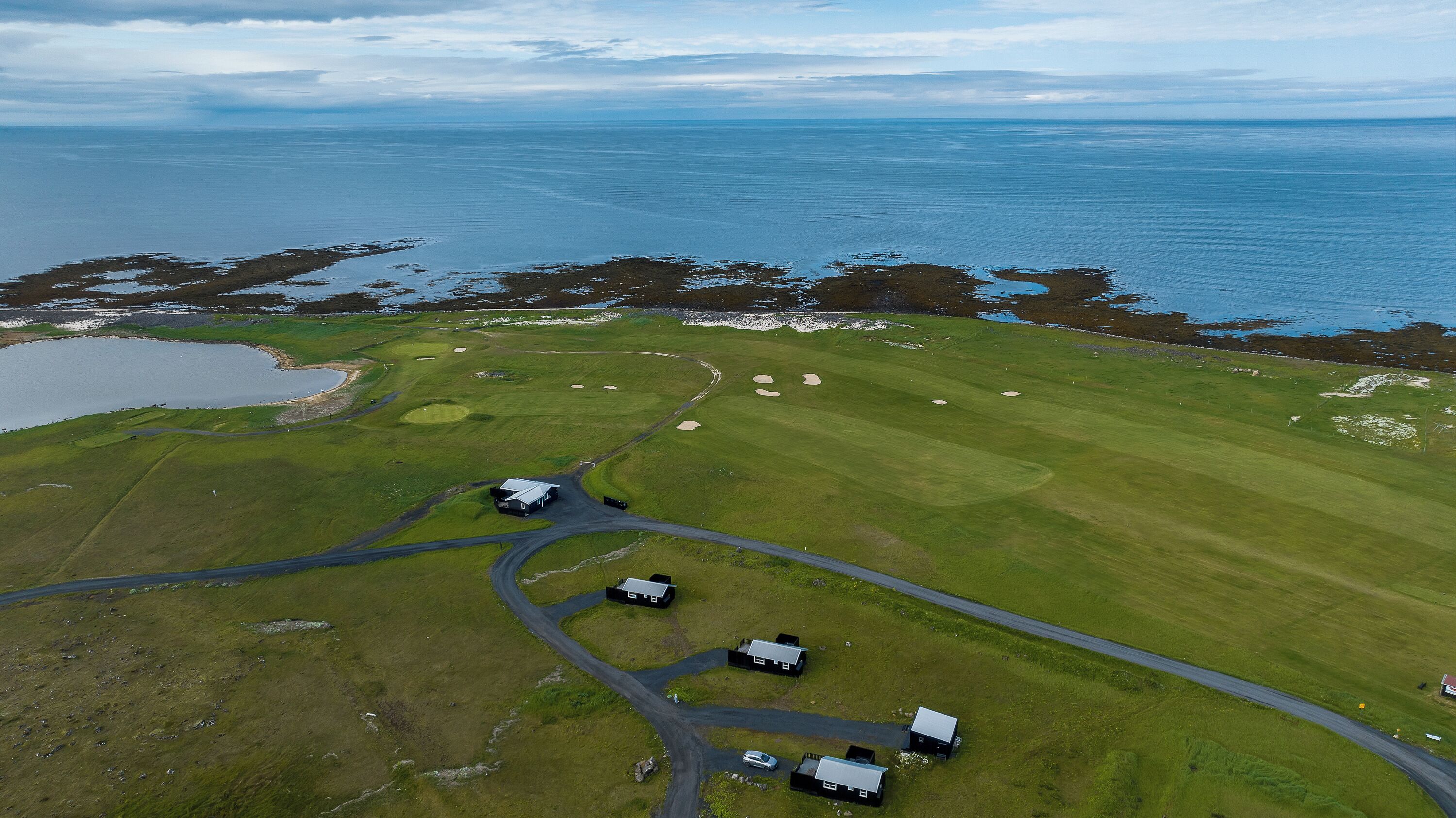 An aerial view of a golf course with a body of water, a small lake, and a few buildings.