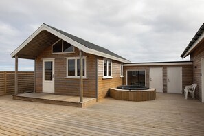A wooden cabin with a covered deck, a hot tub, and a view of the sea. - Ocean Break Cabins (Suðurnesjabær)