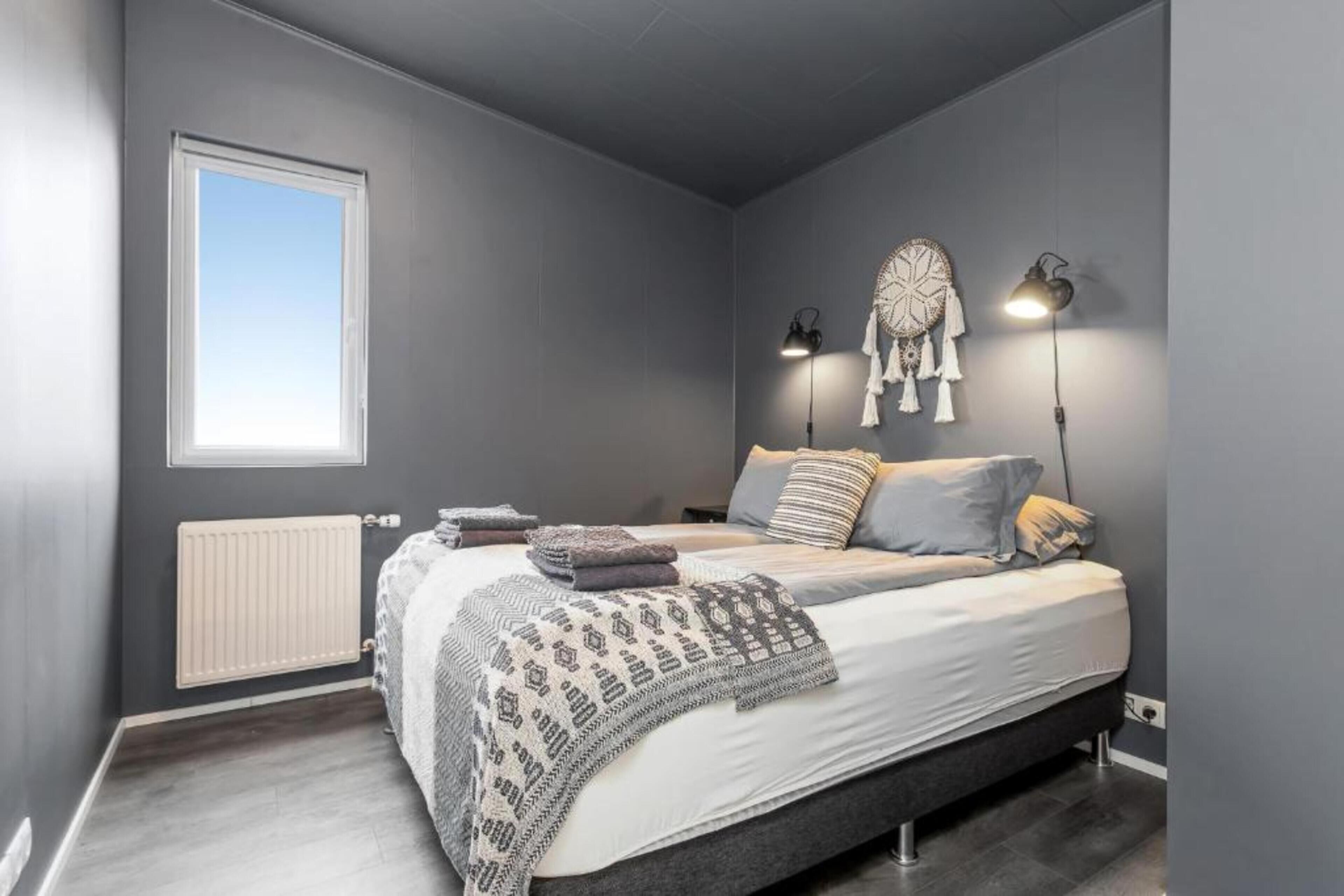 A modern bedroom with a large bed, a radiator, a window, and two wall-mounted lamps.