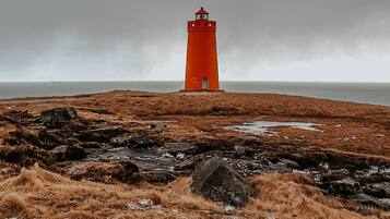 A lighthouse on a rocky, grassy terrain with a cloudy sky.