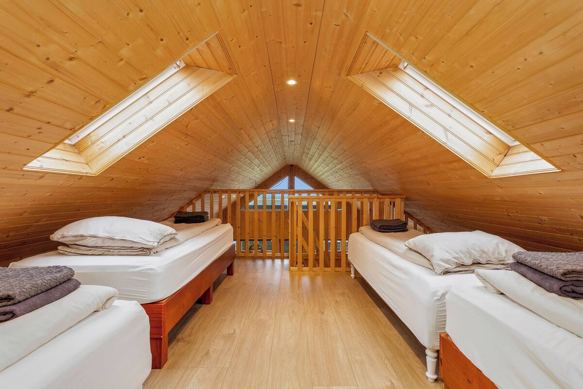 Un dormitorio acogedor en el desván con dos camas, vigas de madera y un tragaluz.