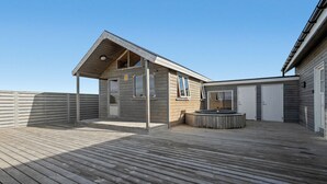 A wooden deck with a covered outdoor area, a hot tub, and a building with a pitched roof. - Ocean Break Cabins (Suðurnesjabær)