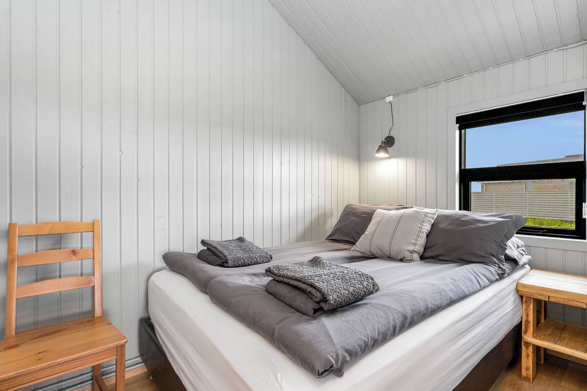 Un dormitorio con cama, una silla de madera, una mesita y una ventana con vistas al exterior.