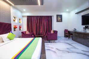 A hotel room with a large bed, a desk, two chairs, a television, and a decorative wall.