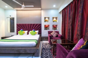 A modern hotel room with a large bed, a purple armchair, a small table, and decorative wall panels.