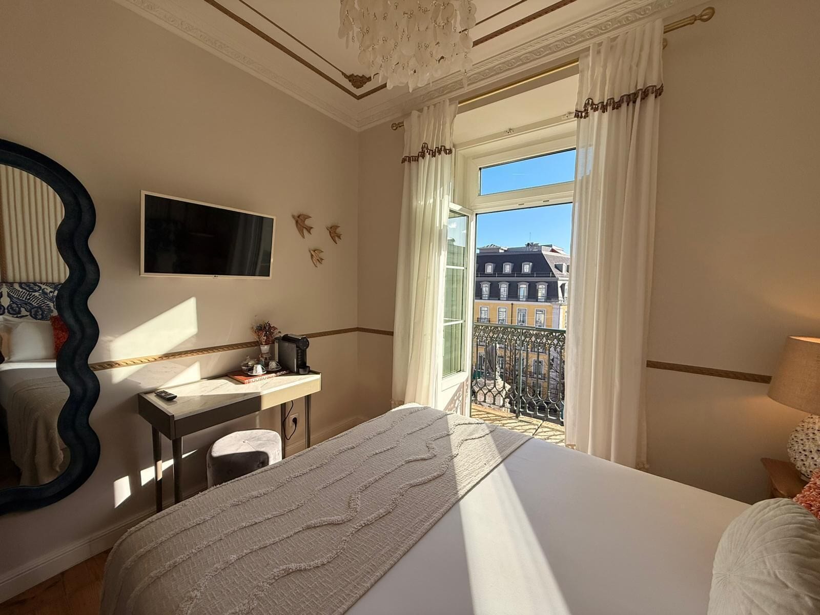 Habitación de hotel con una cama grande, un escritorio, una silla, un televisor y un balcón con vistas a edificios.