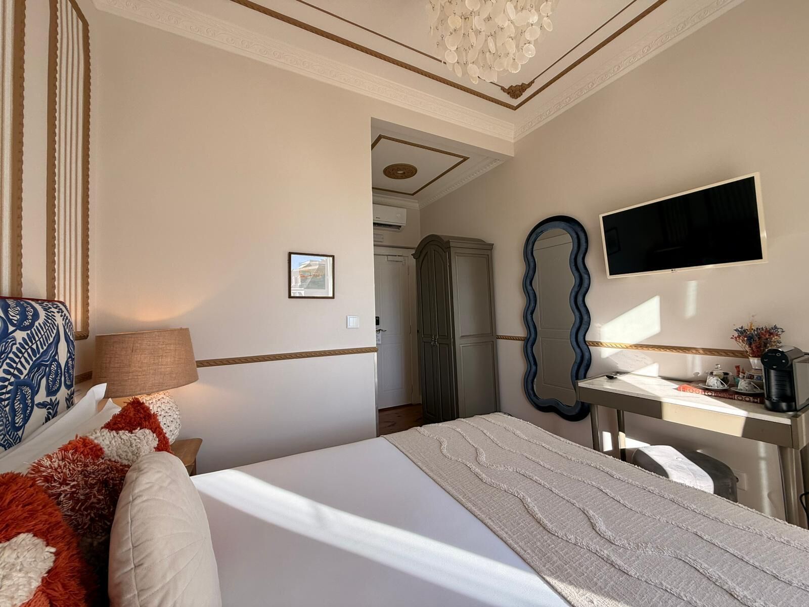 A hotel room with a bed, a desk, a mirror, a television, and a wardrobe.