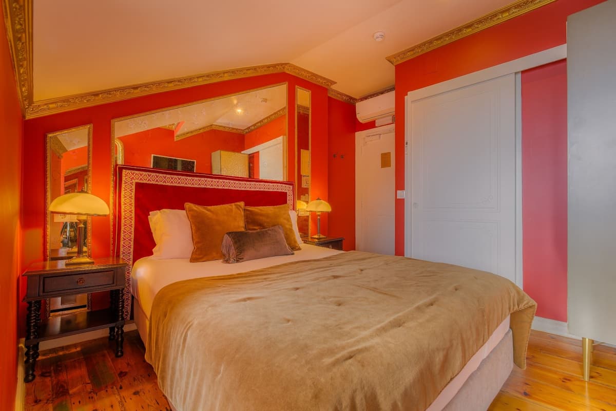 Une chambre à coucher avec un grand lit, deux tables de chevet avec des lampes, un miroir au-dessus du lit et une porte blanche.