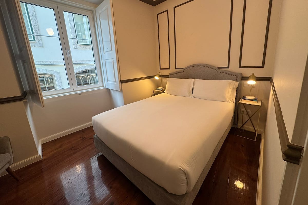 Une chambre à coucher bien aménagée, avec un grand lit, deux tables de chevet avec des lampes, une fenêtre avec des rideaux et un plancher en bois.