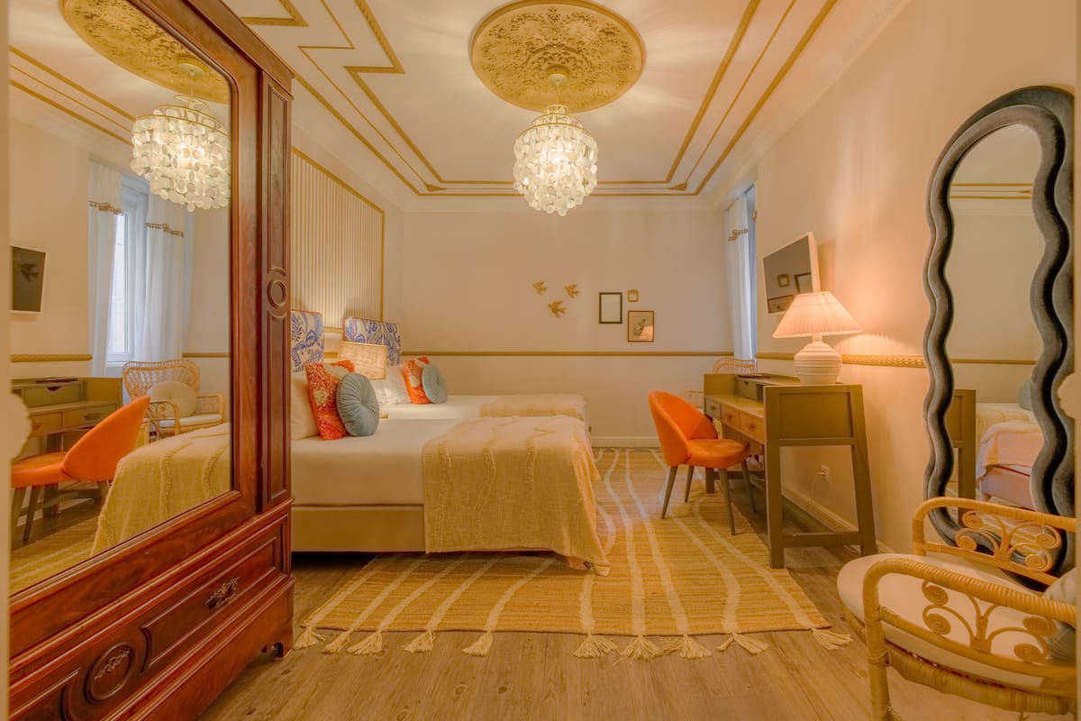 Une chambre à coucher avec un grand miroir, un lit recouvert d’une couvre-lit à motifs, une commode et une chaise.