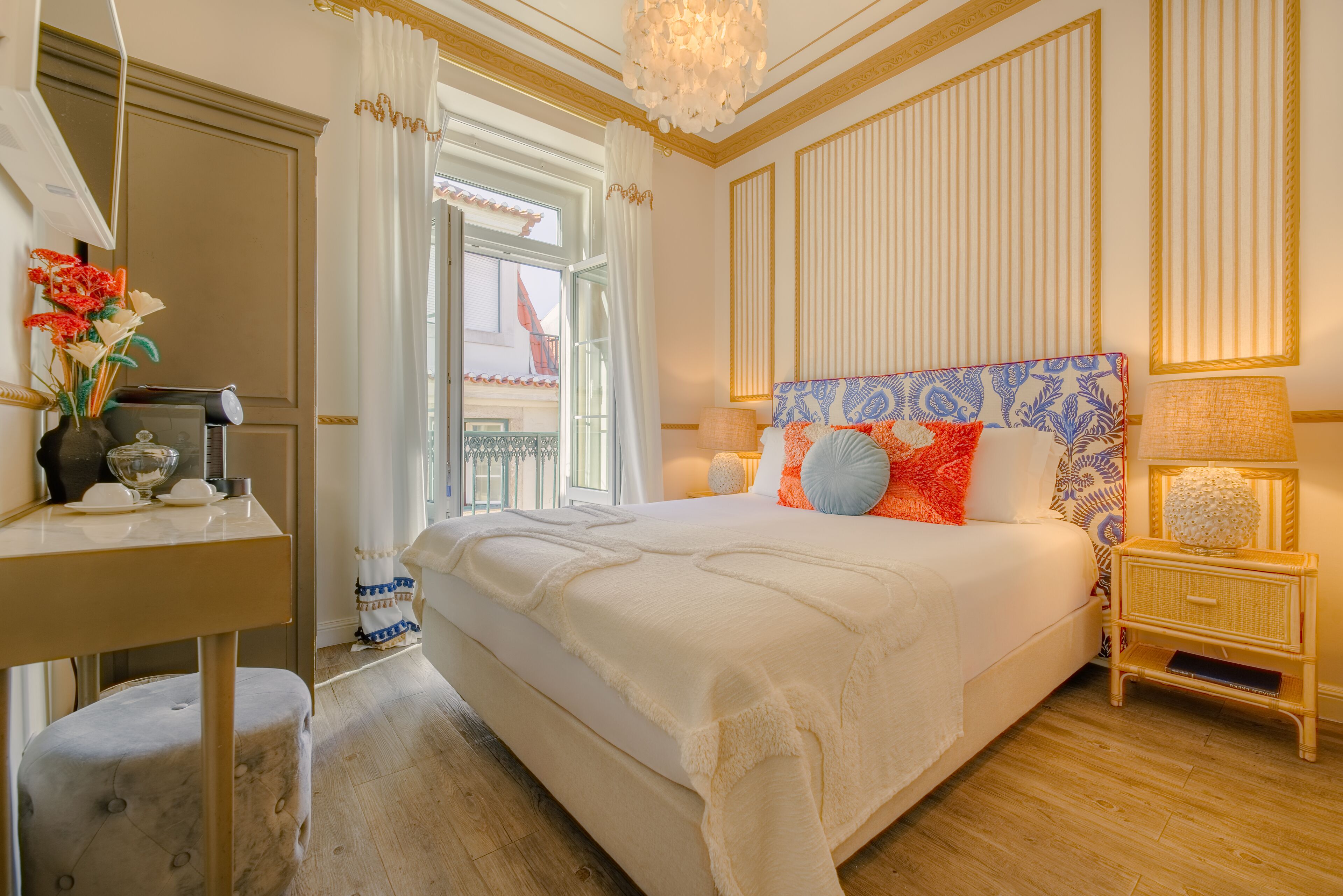 A well-lit bedroom with a large bed, a bedside table with a lamp, and a view of the outside balcony.