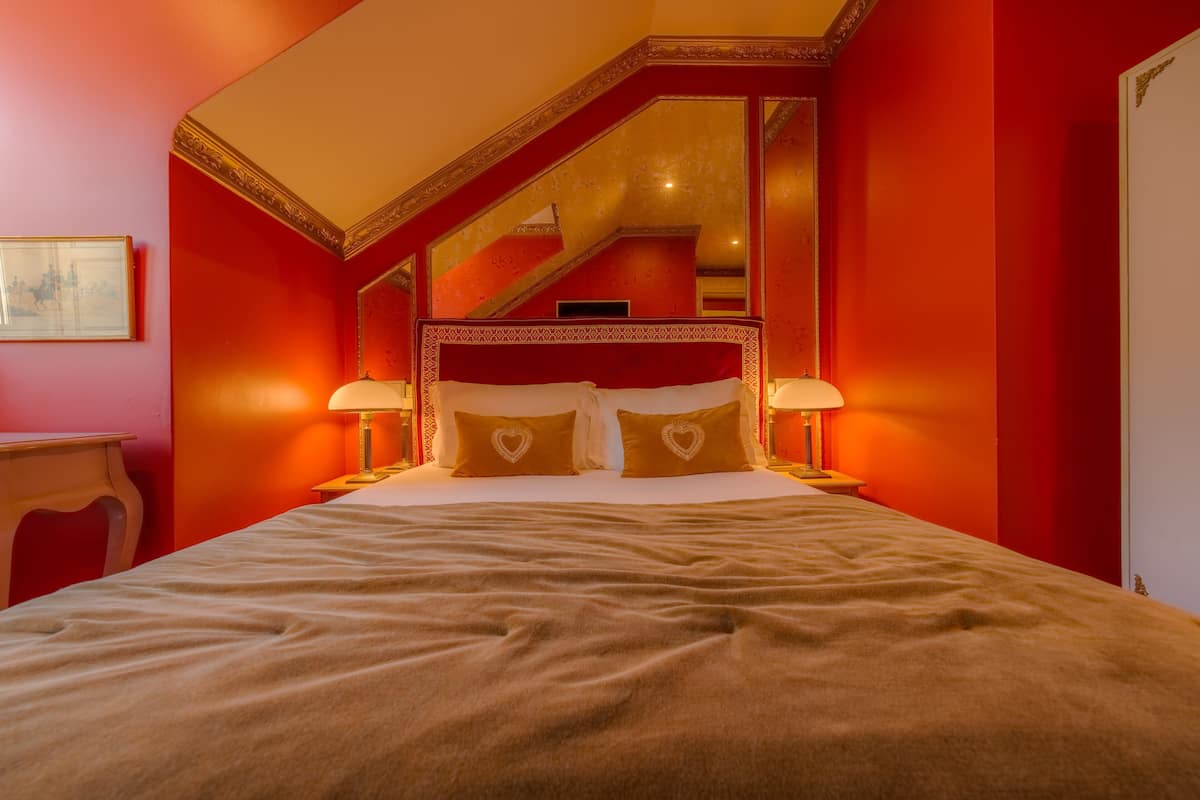 Un grand lit avec une tête de lit rouge, deux lampes de chevet et un miroir au-dessus du lit.