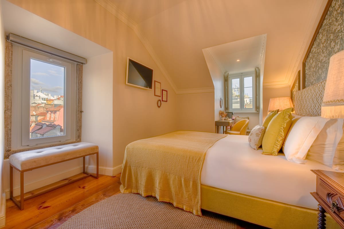 Une chambre à coucher avec un grand lit, un banc, une fenêtre et un miroir.