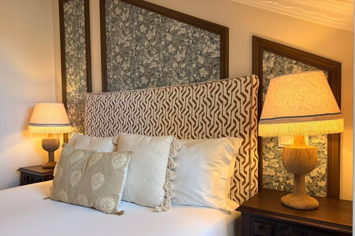 Un lit bien fait, agrémenté d’oreillers à motifs, de deux lampes de chevet et d’un panneau décoratif mural.