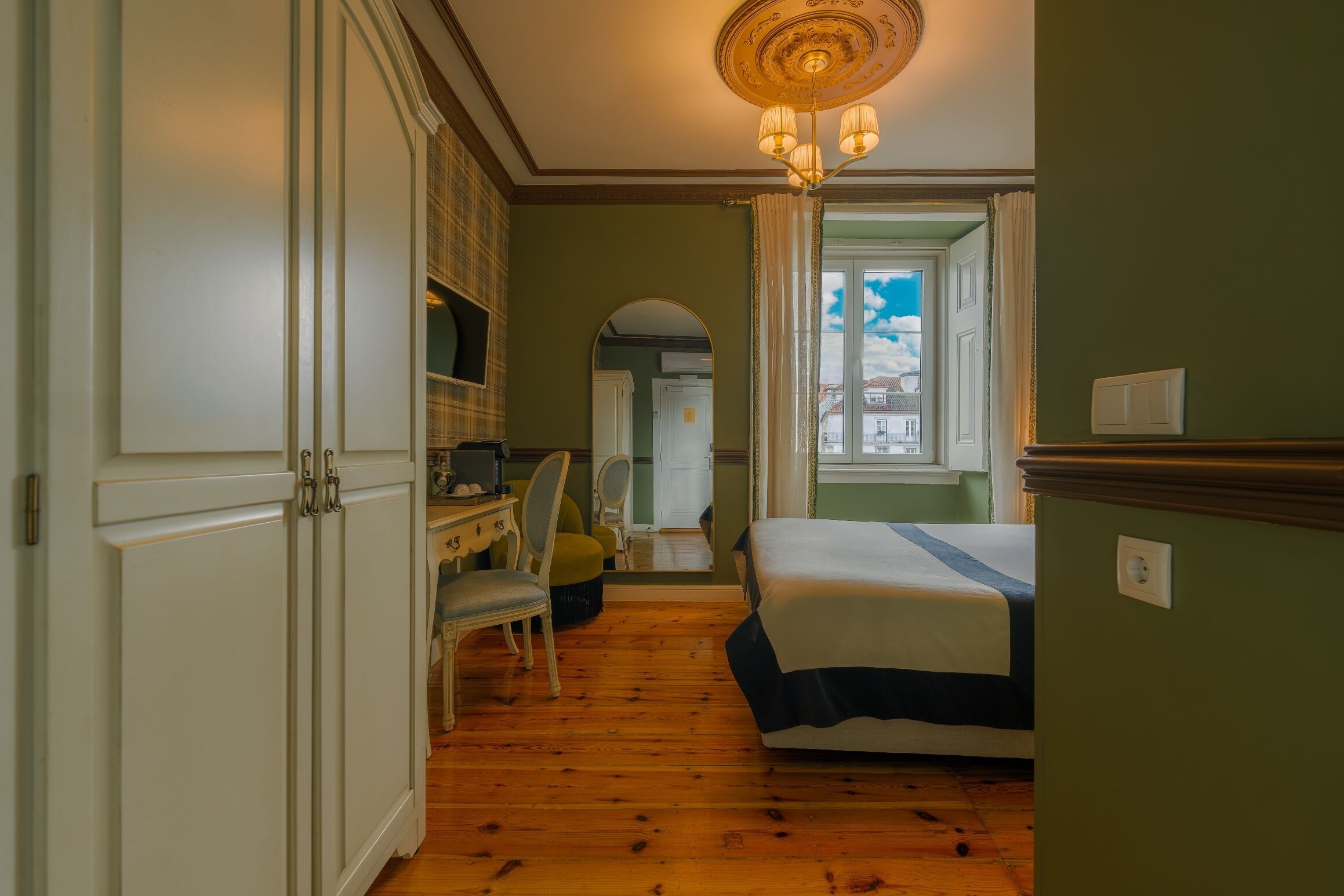 Un dormitorio con cama, escritorio, silla, televisor y ventana con cortinas.