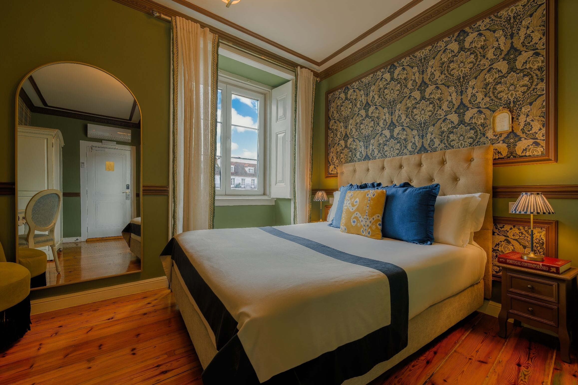 Une chambre avec un grand lit, un miroir, une fenêtre et un mur décoré de motifs.
