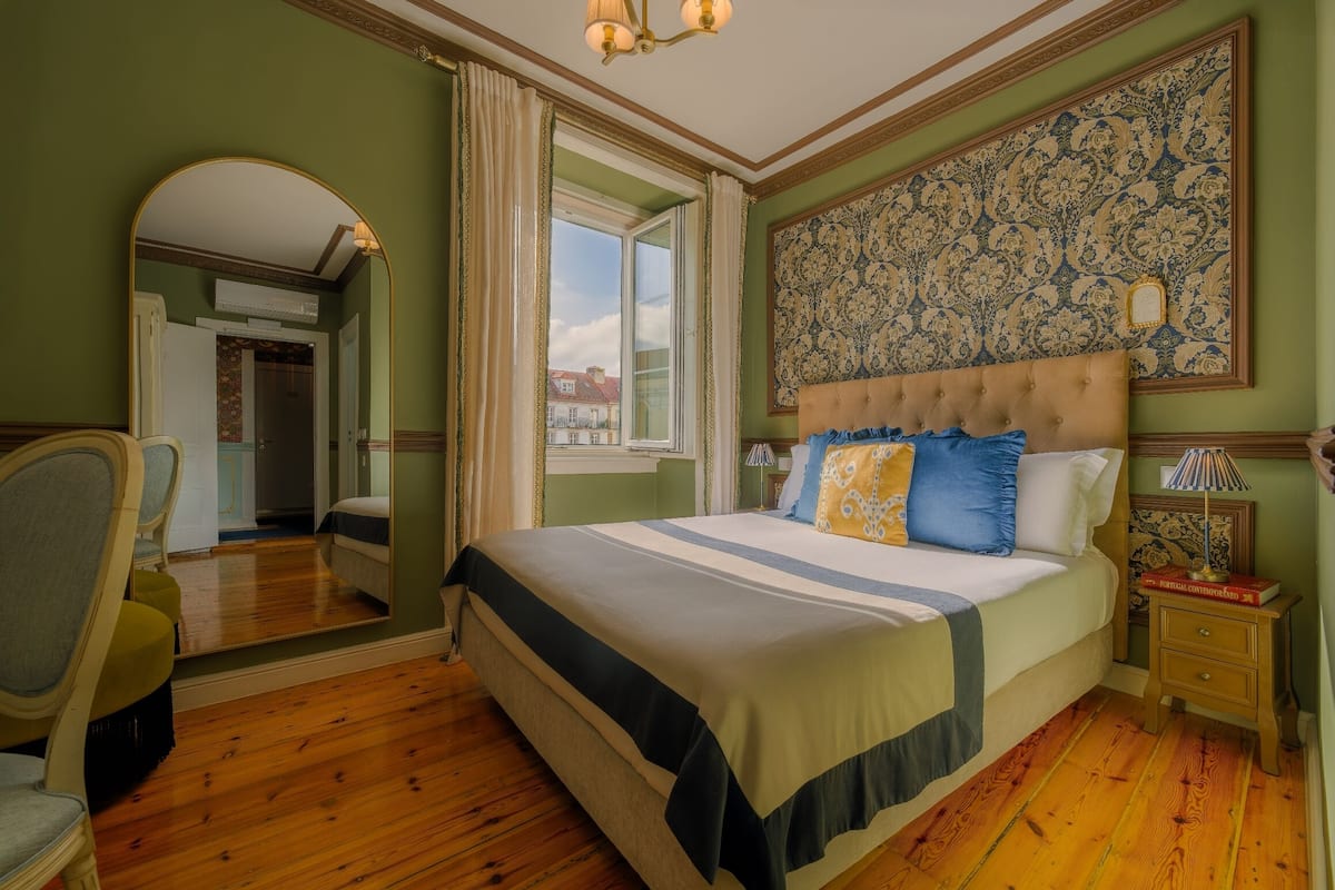 Une chambre à coucher avec un grand lit, un miroir, une table de chevet et une fenêtre avec des rideaux.