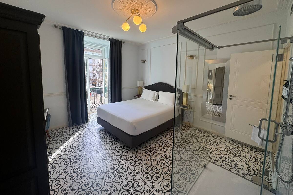 Une chambre d’hôtel avec un lit, une cabine de douche en verre et des carreaux de sol à motifs.