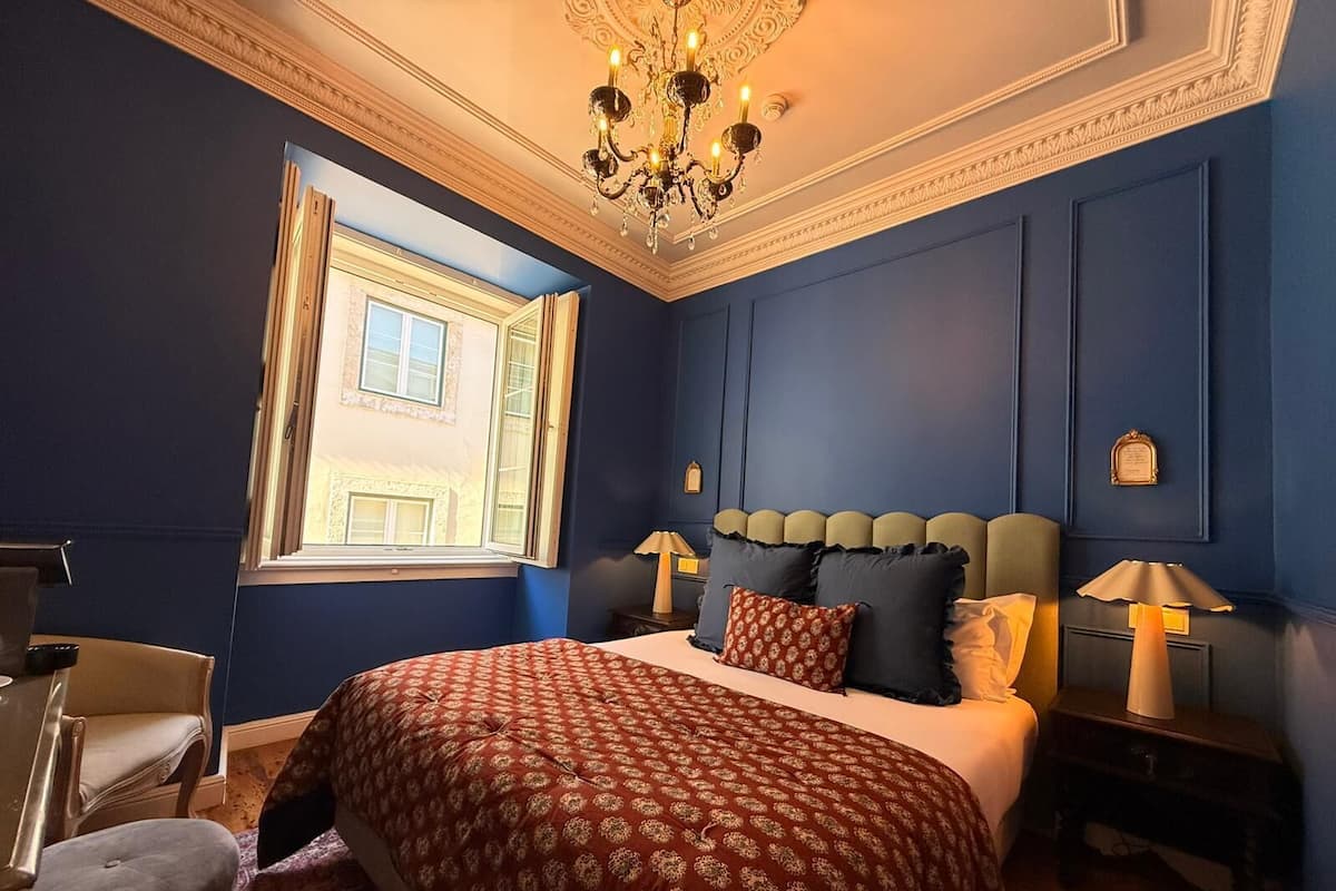 Une chambre à coucher avec un grand lit, deux tables de chevet avec des lampes, une chaise, une fenêtre et un lustre.