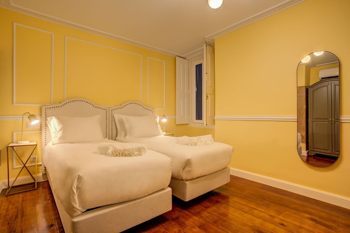 Une chambre avec deux lits, un plancher en bois et un miroir au mur.