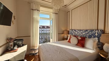 Quarto de hotel com uma cama grande, uma escrivaninha com cadeira, televisão e varanda com cortinas.