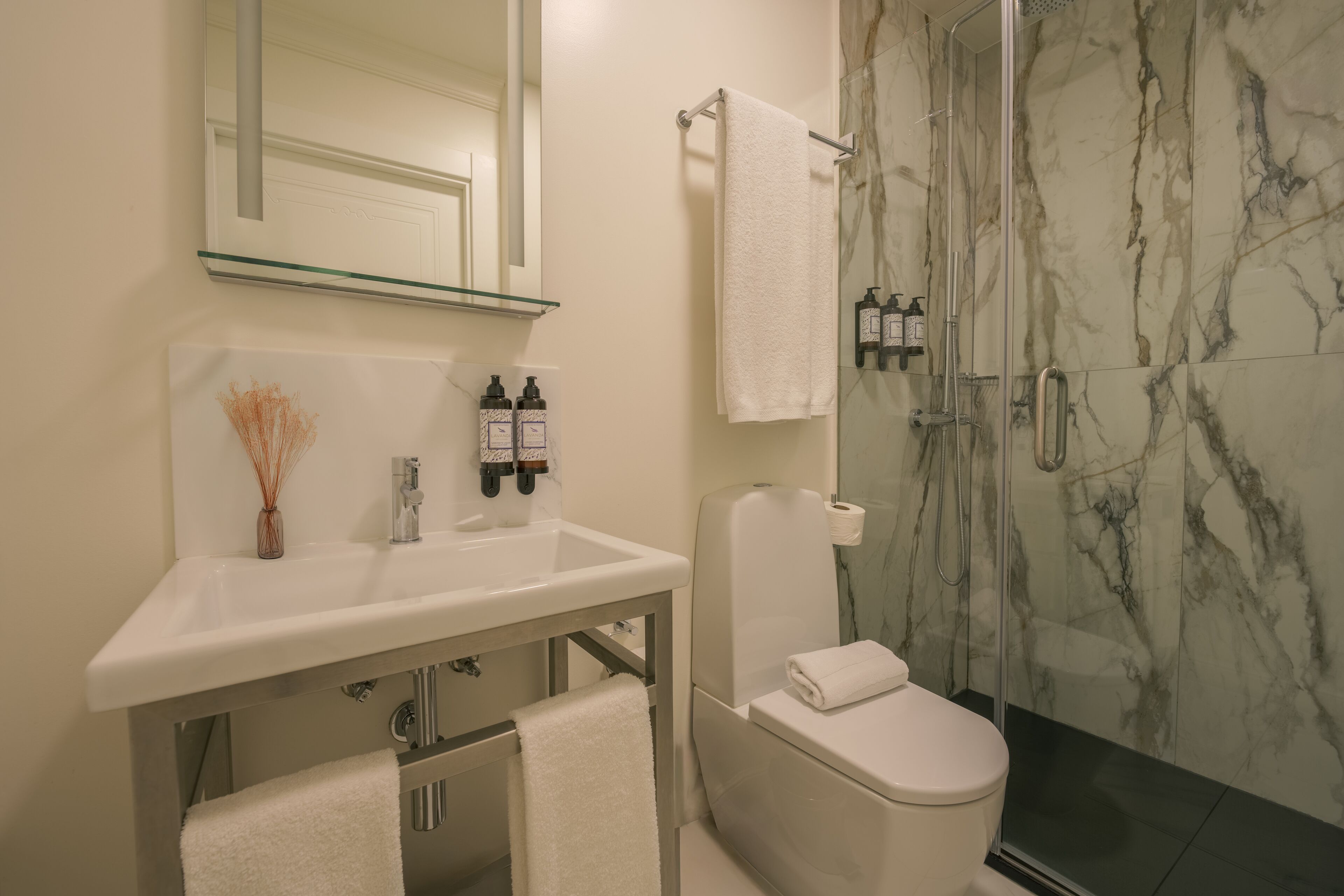 Un baño moderno con cabina de ducha de vidrio, lavamanos blanco y retrete.