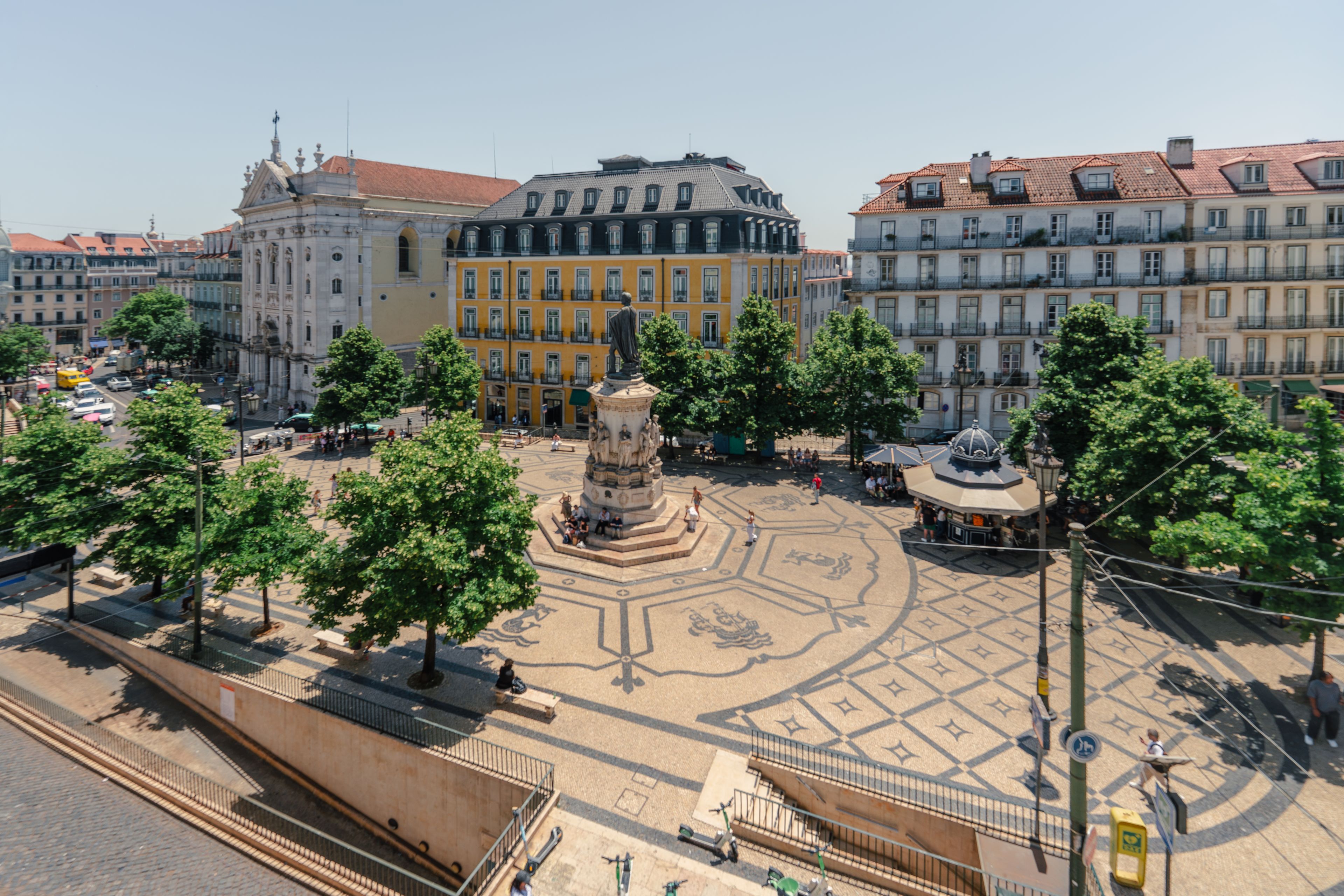 A square with a central monument, surrounded by trees and buildings with varied architectural styles.