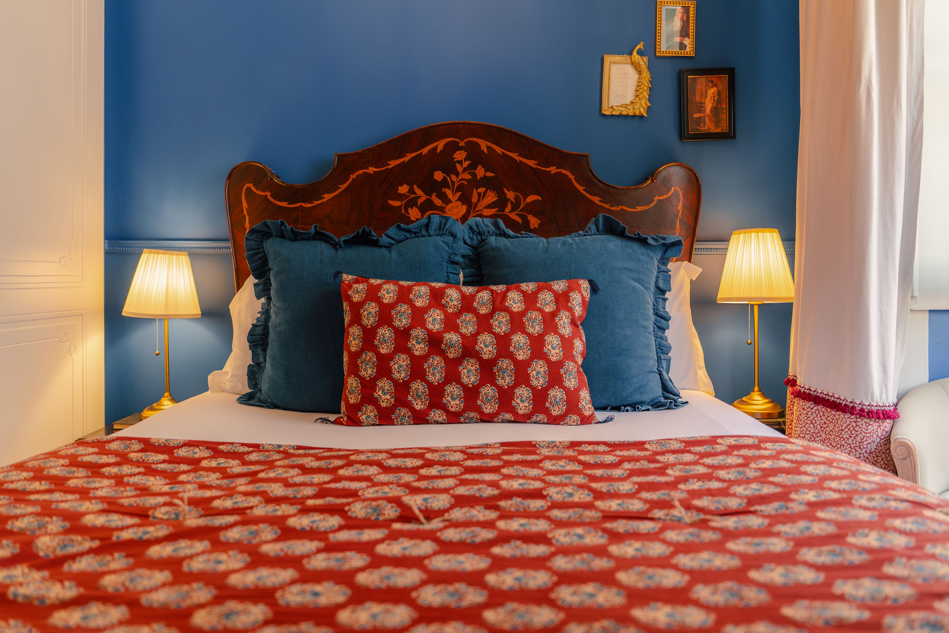 Una cama con colcha estampada floral, dos almohadas con flecos y dos lámparas de noche.