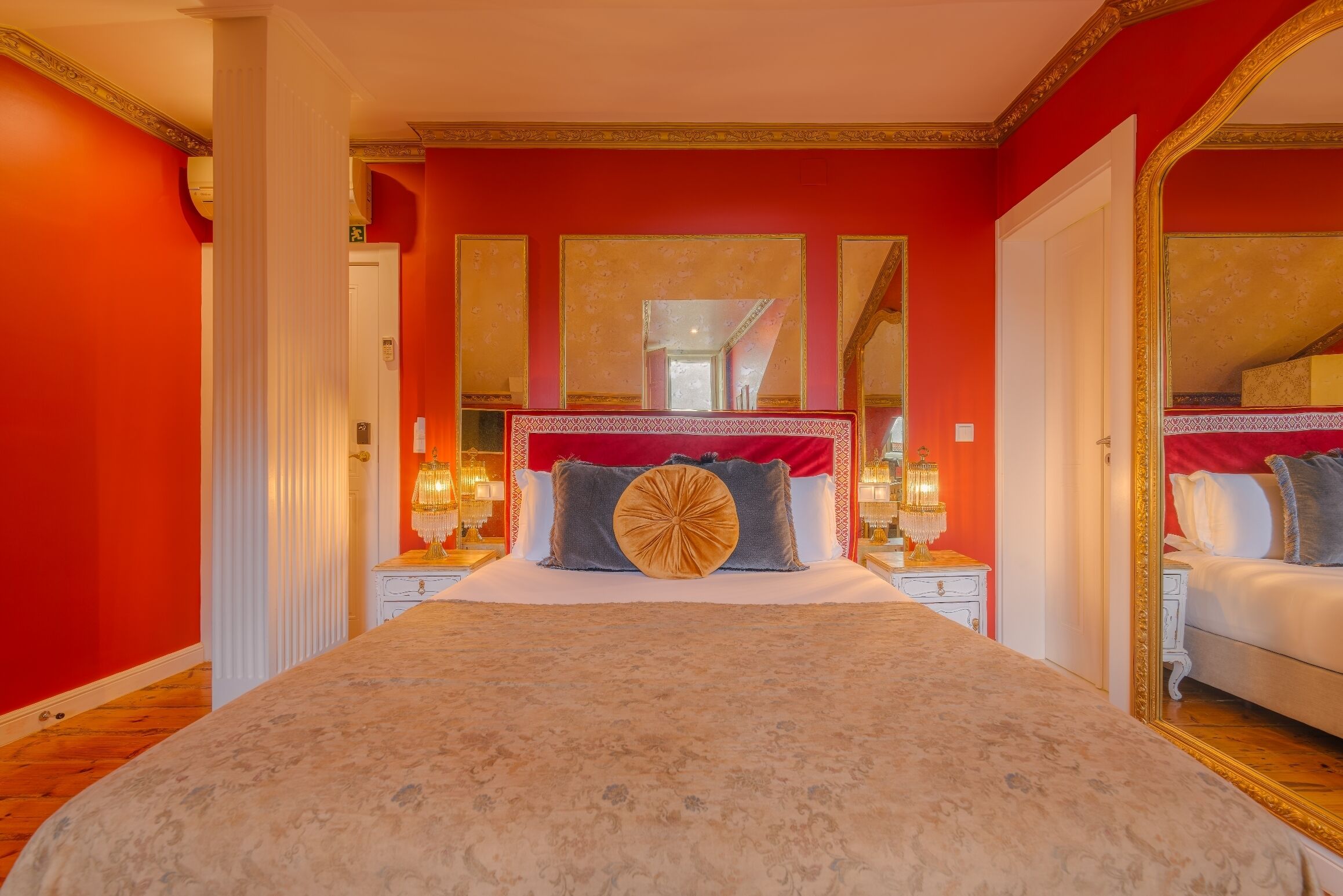A large bed with a patterned bedspread, two bedside tables with lamps, and a large mirror above the bed.
