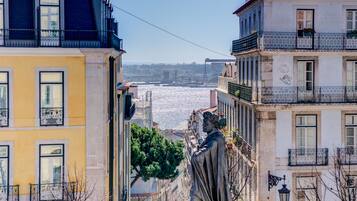 A statue in a square surrounded by buildings with balconies and a view of the sea.