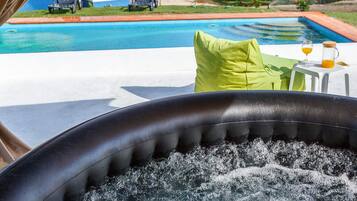 A hot tub with a view of a swimming pool and outdoor seating area.