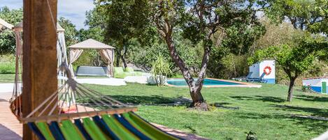 Uma rede em um deck de madeira, uma piscina e um gazebo em um quintal.
