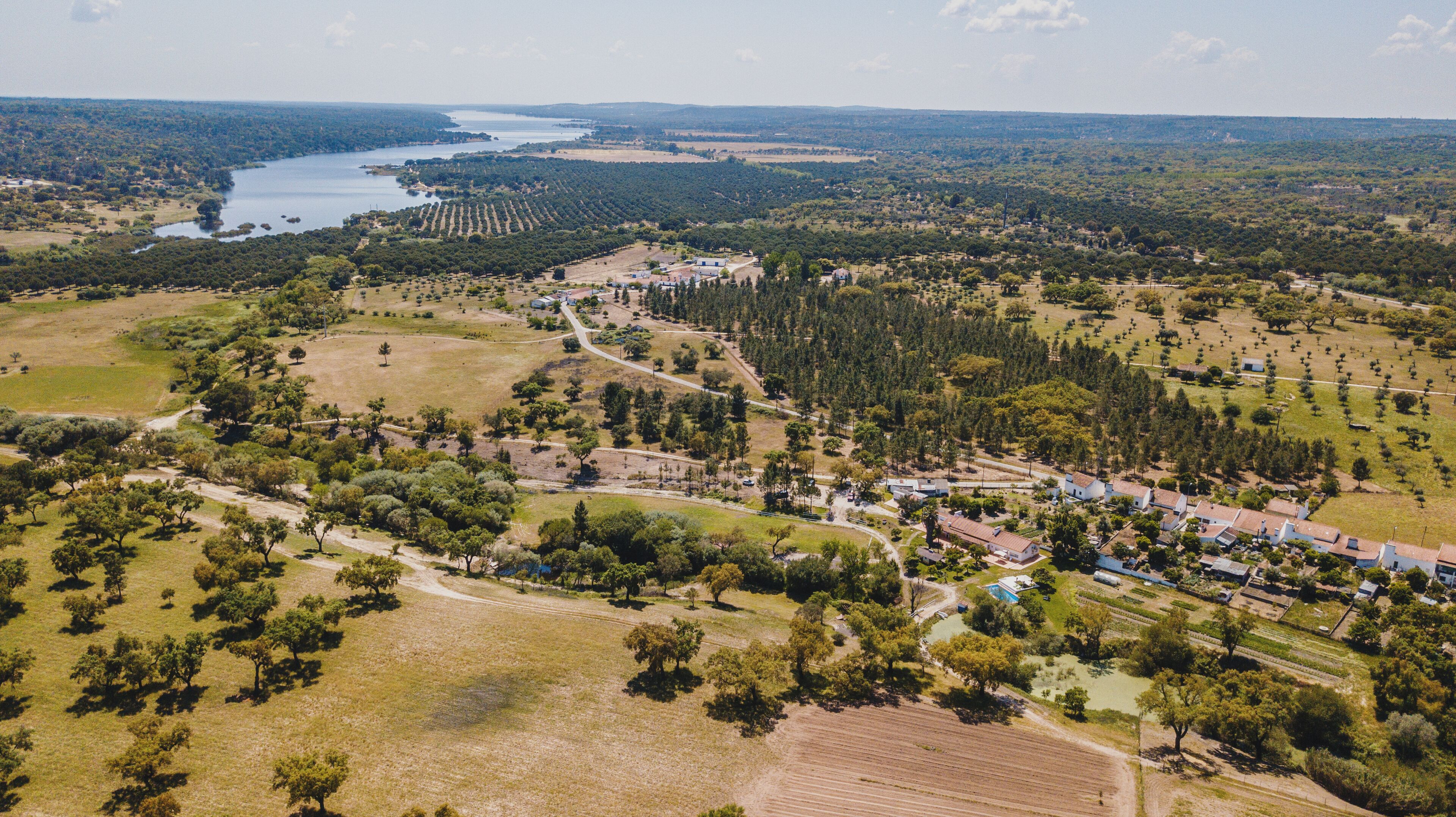 Vista aérea de uma área rural com campos, árvores e um pequeno povoado.