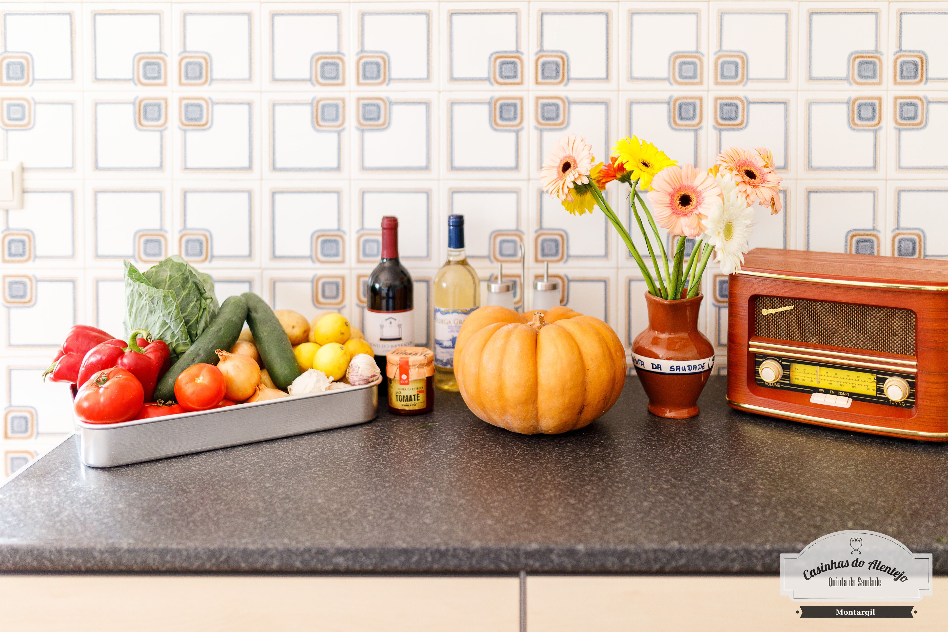 Una encimera de cocina con una variedad de frutas y verduras frescas, una calabaza, una radio y un jarrón con flores.
