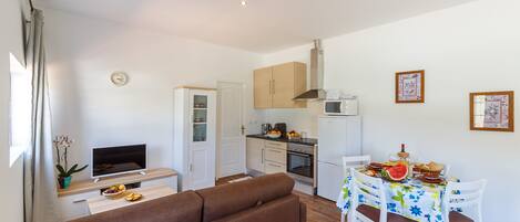 A compact living space with a sofa, dining table, kitchen area, and a TV.