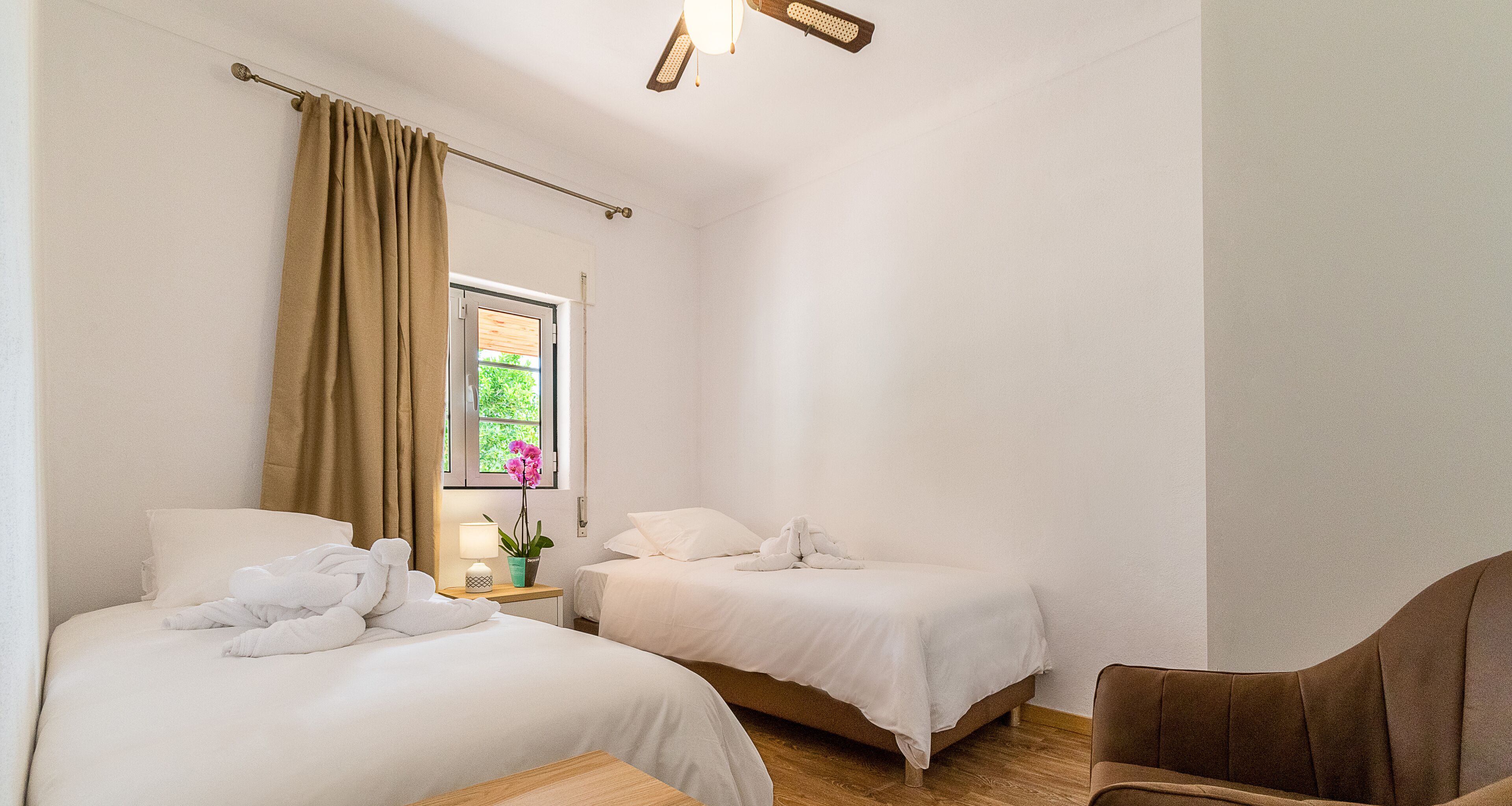 Quarto de hotel com duas camas, janela com cortinas, uma mesa pequena com abajur e uma cadeira.