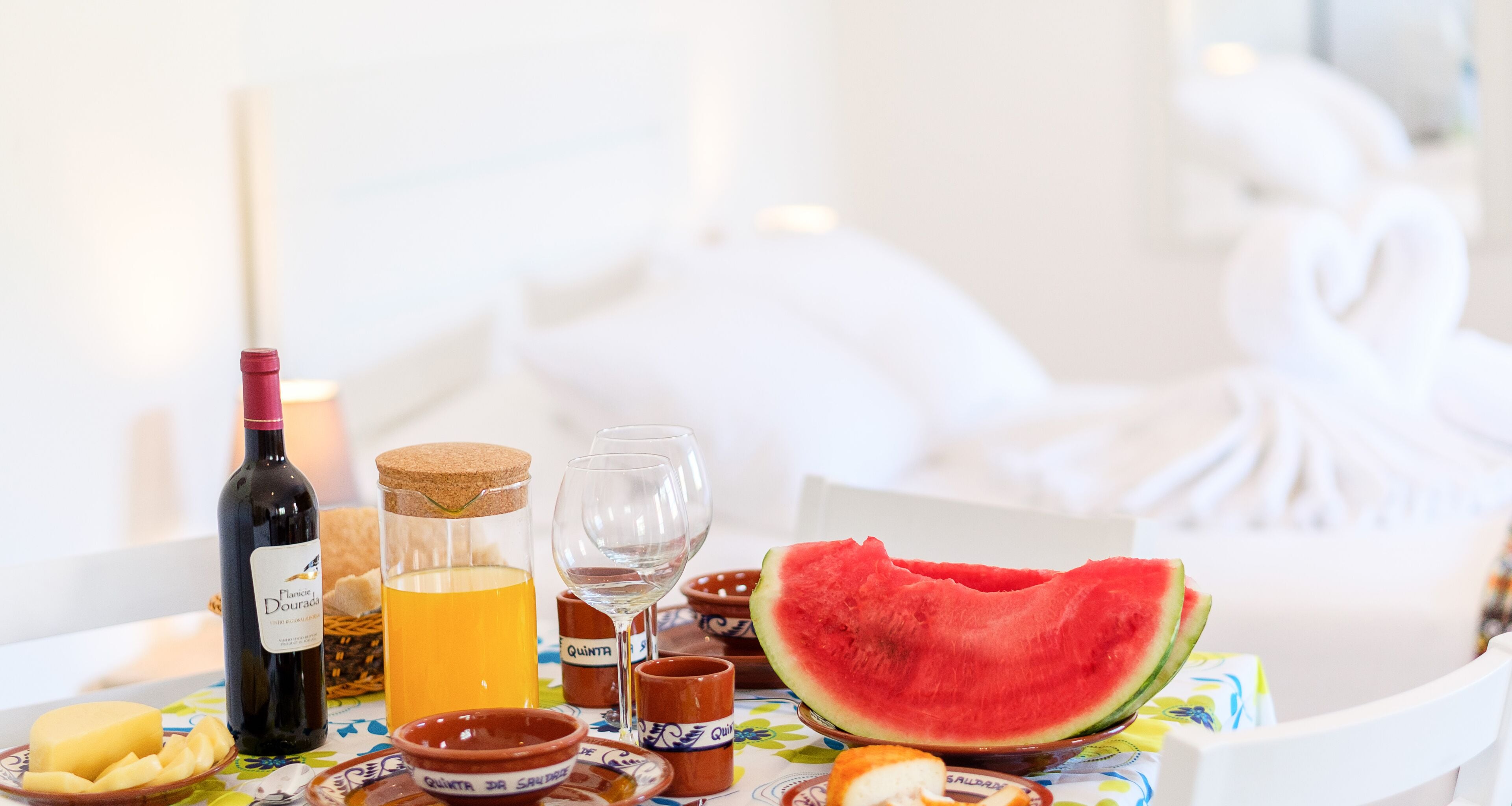 A table with a bottle of wine, a glass of orange juice, a glass of water, a slice of watermelon, and small bowls with snacks.