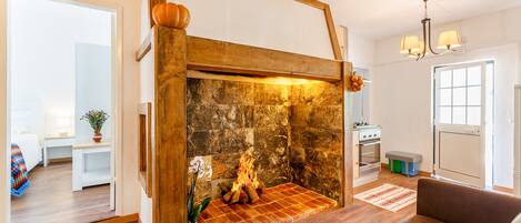 A cozy living room with a fireplace, wooden flooring, a sofa, and a dining area with a table and chairs.
