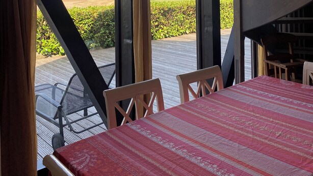 Een eethoek met een tafel voor vier personen, grote ramen en uitzicht op een groen landschap.