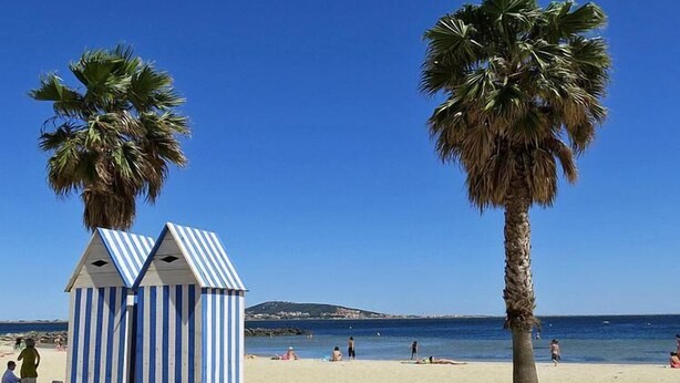 Uma praia com cabanas listradas, palmeiras e um céu azul límpido.