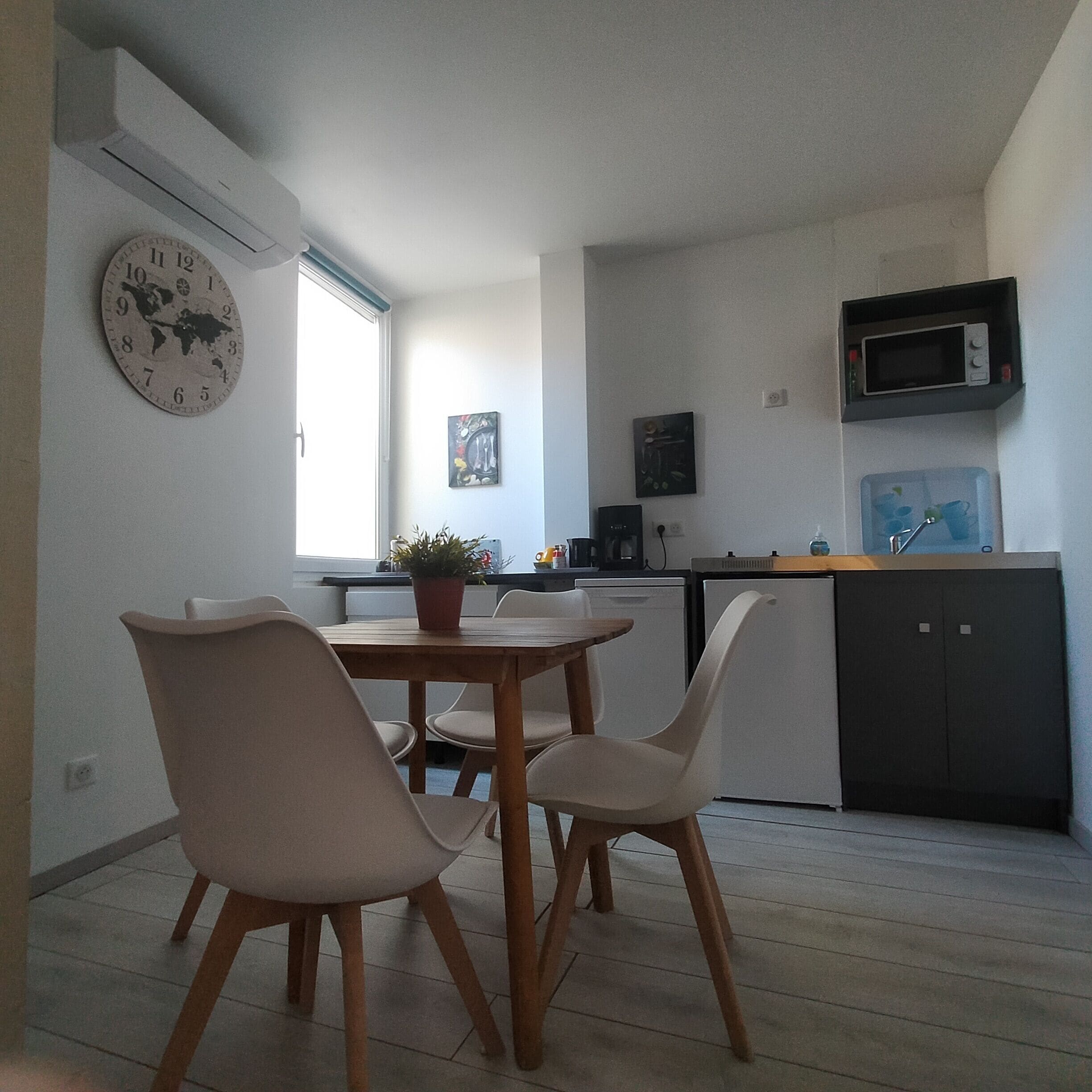 Une cuisine moderne avec un coin repas, comprenant une table et des chaises en bois, une horloge et un four à micro-ondes.