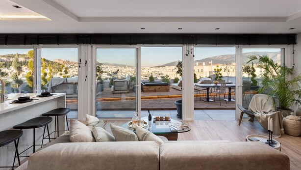Una sala de estar moderna con un ventanal grande, un sofá, una mesa de centro y vistas a un paisaje urbano.